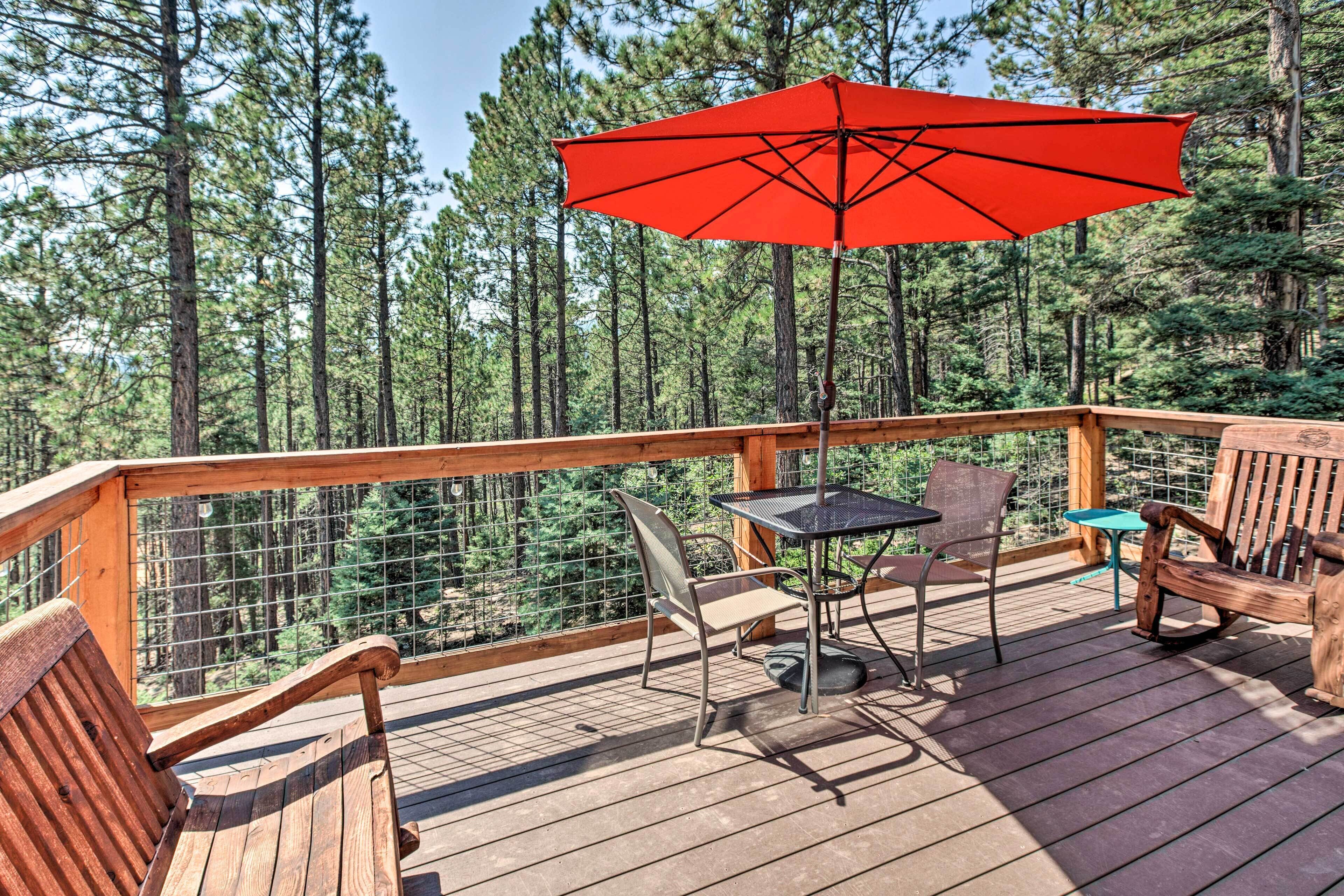 Une terrasse en bois avec une table, des chaises et un parasol rouge.