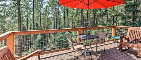 Une terrasse en bois avec une table, des chaises et un parasol rouge.