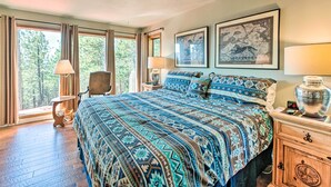 A bedroom with a large bed, a chair, a nightstand, and a window with curtains. - Hot Tub, Game Room: Spacious Angel Fire Retreat! (Angel Fire)