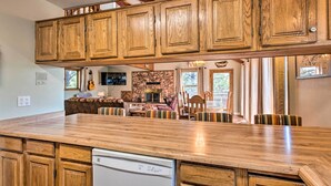 A kitchen with wooden cabinets, a built-in dishwasher, and a dining area with striped chairs. - Hot Tub, Game Room: Spacious Angel Fire Retreat! (Angel Fire)