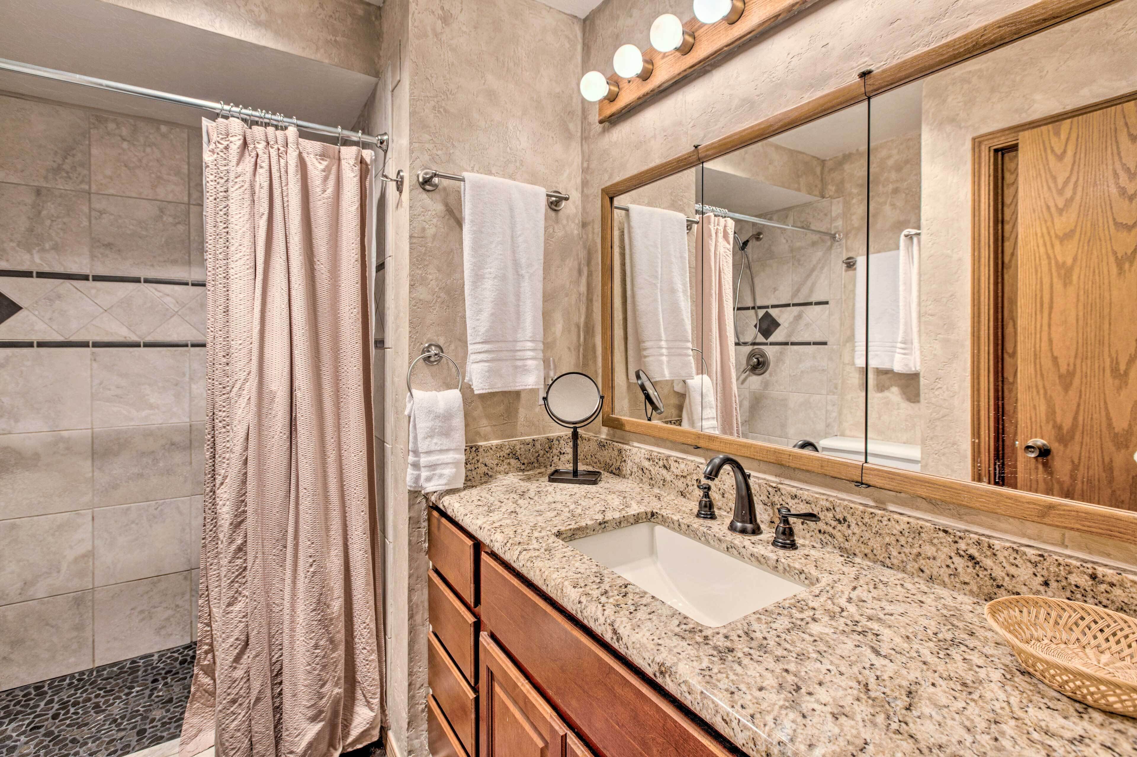 Une salle de bain avec un lavabo sur un plan de travail en granit, un meuble-lavabo en bois, un grand miroir et un rideau de douche.