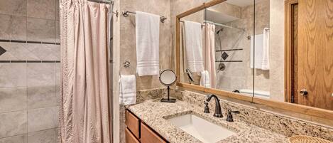Une salle de bain avec un lavabo sur un plan de travail en granit, un meuble-lavabo en bois, un grand miroir et un rideau de douche.