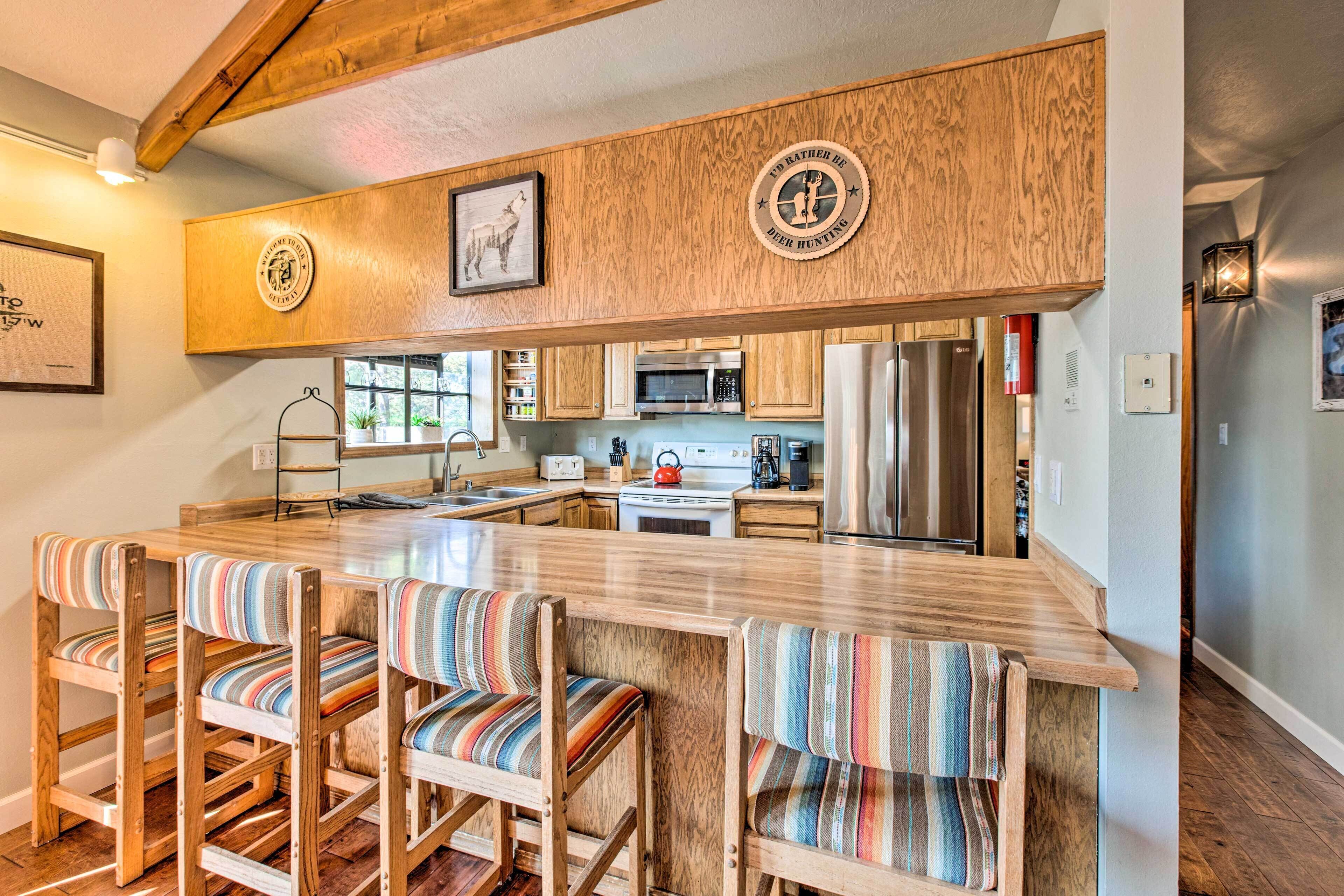A kitchen with wooden bar stools, a stainless steel refrigerator, and a microwave.