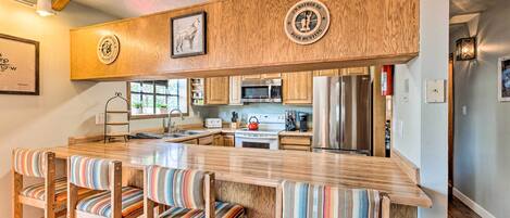 A kitchen with wooden bar stools, a stainless steel refrigerator, and a microwave.