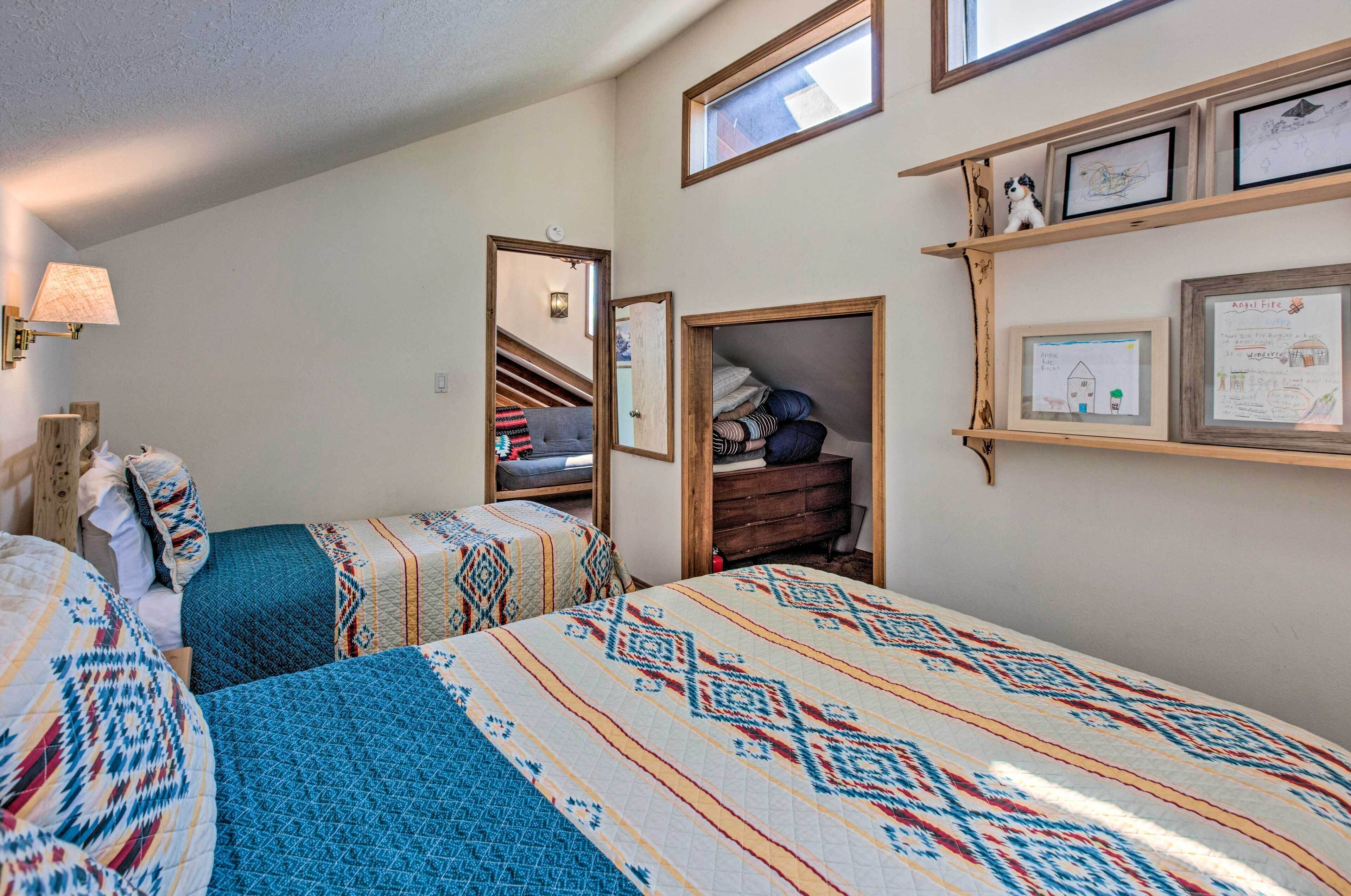 A bedroom with two beds, a dresser, a mirror, and a shelf with framed artwork.
