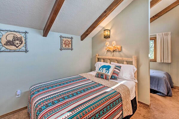 Un dormitorio con cama, mesita de noche, lámpara de pared y dos cuadros.
