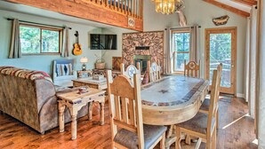 A cozy living room with a stone fireplace, wooden dining table, and a high ceiling with exposed beams. - Hot Tub, Game Room: Spacious Angel Fire Retreat! (Angel Fire)