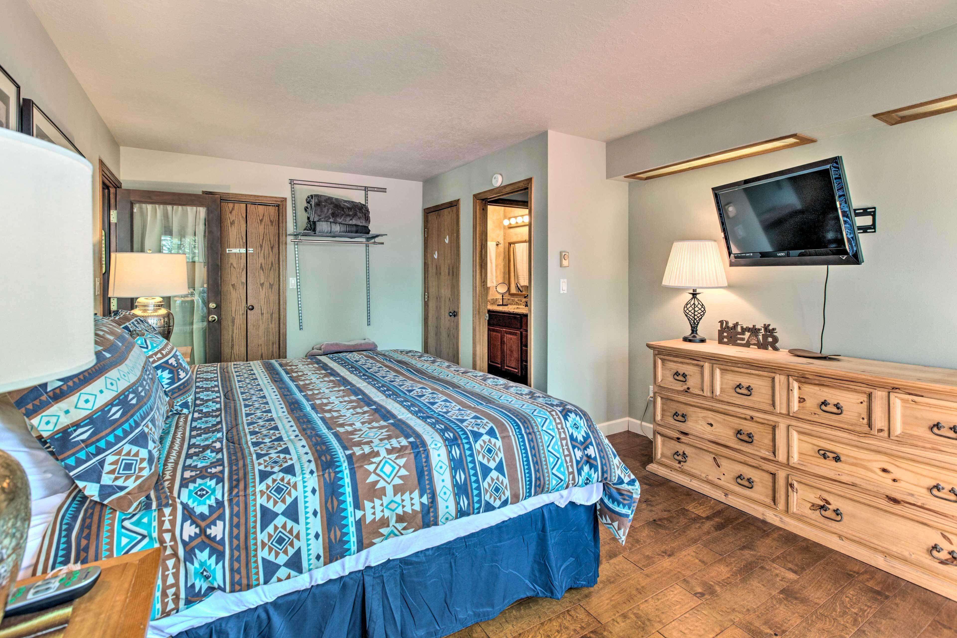 A bedroom with a large bed, wooden dresser, and a mounted TV.