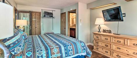 A bedroom with a large bed, wooden dresser, and a mounted TV.