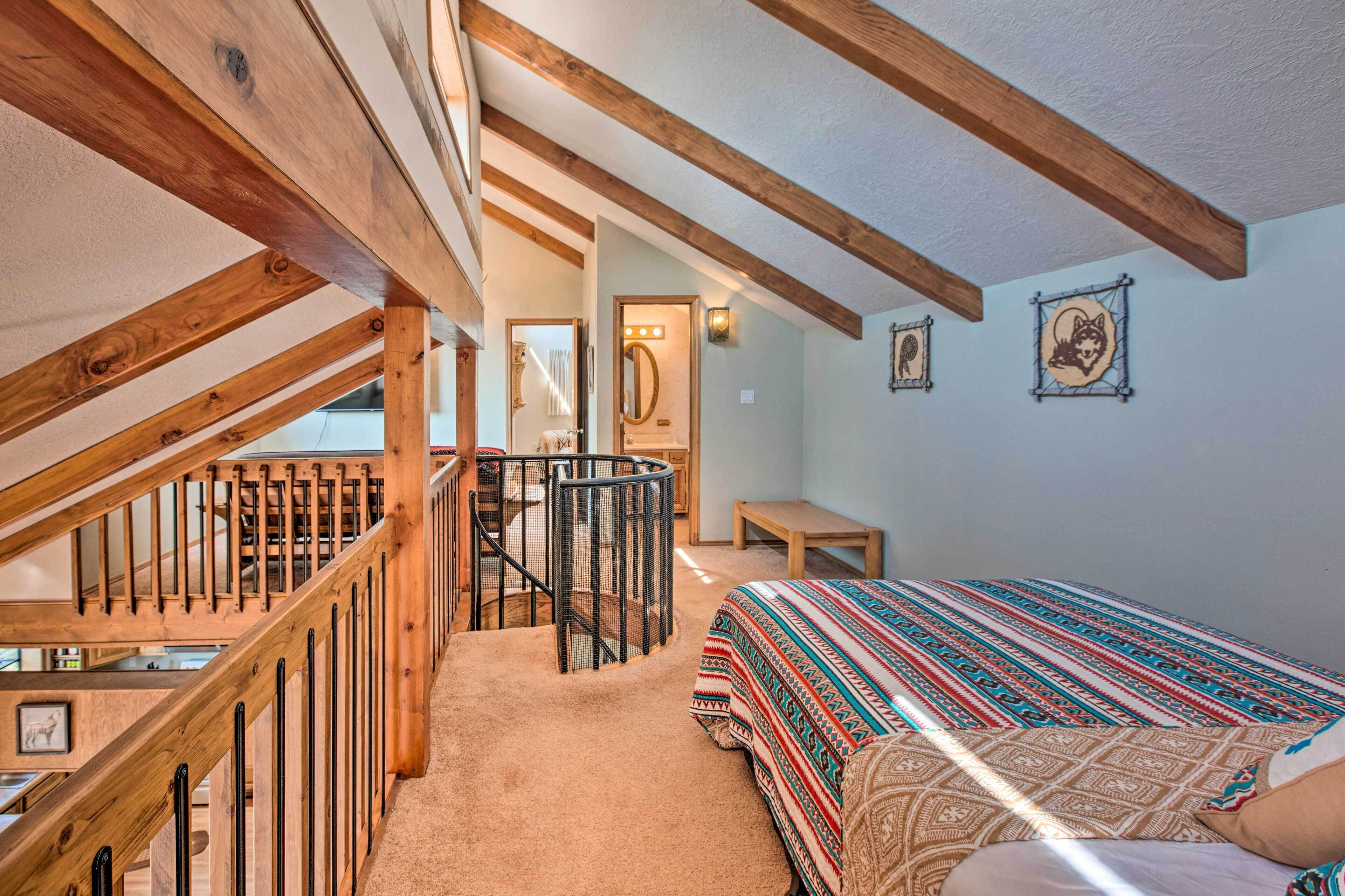Ein Schlafzimmer mit einer Holztreppe, einem Bett mit gemusterten Textilien, einem kleinen Tisch und einem an der Wand befestigten Spiegel.