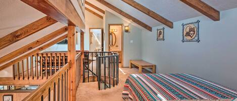 Ein Schlafzimmer mit einer Holztreppe, einem Bett mit gemusterten Textilien, einem kleinen Tisch und einem an der Wand befestigten Spiegel.