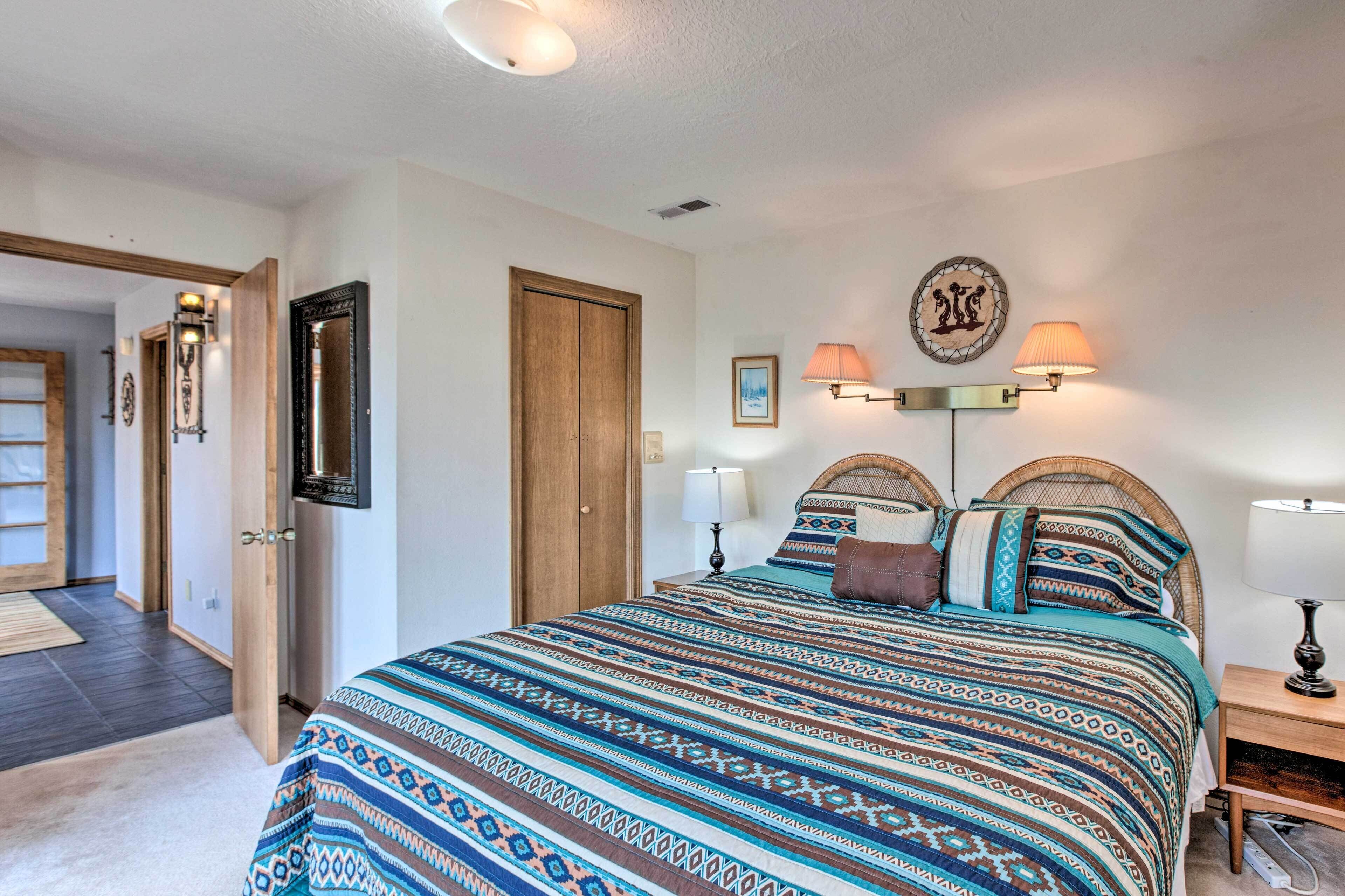 A bedroom with a large bed, two bedside lamps, a door, and a wall-mounted light fixture.