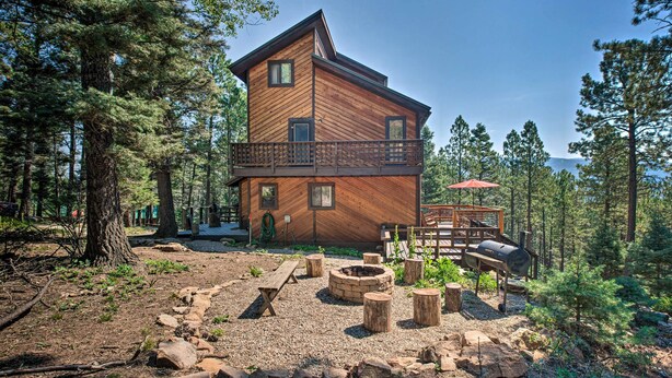 A wooden cabin with a balcony, surrounded by trees and a fire pit area. - Hot Tub, Game Room: Spacious Angel Fire Retreat! (Angel Fire)