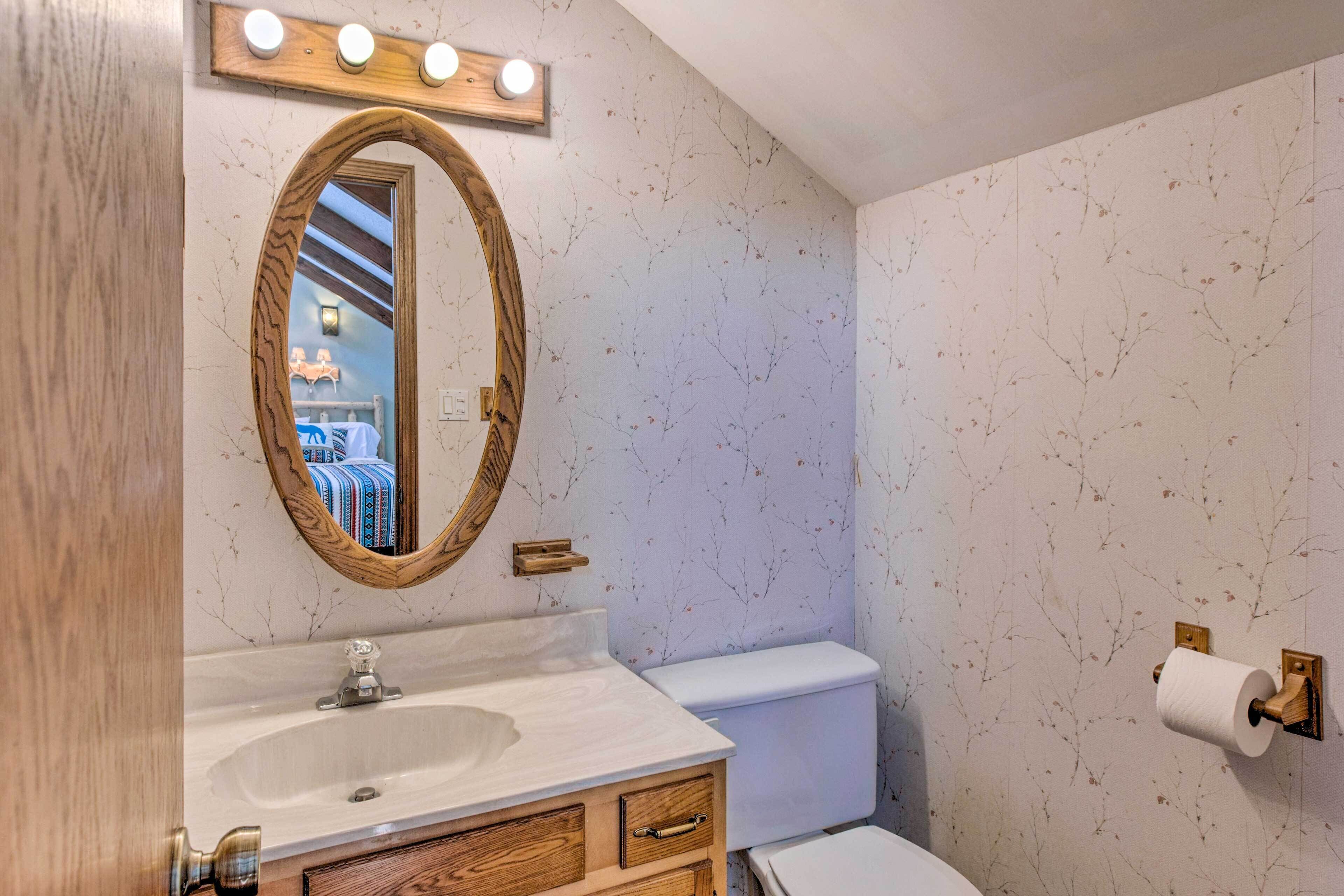 A bathroom with a wooden vanity, a round mirror, a toilet, and a wall-mounted toilet paper holder.