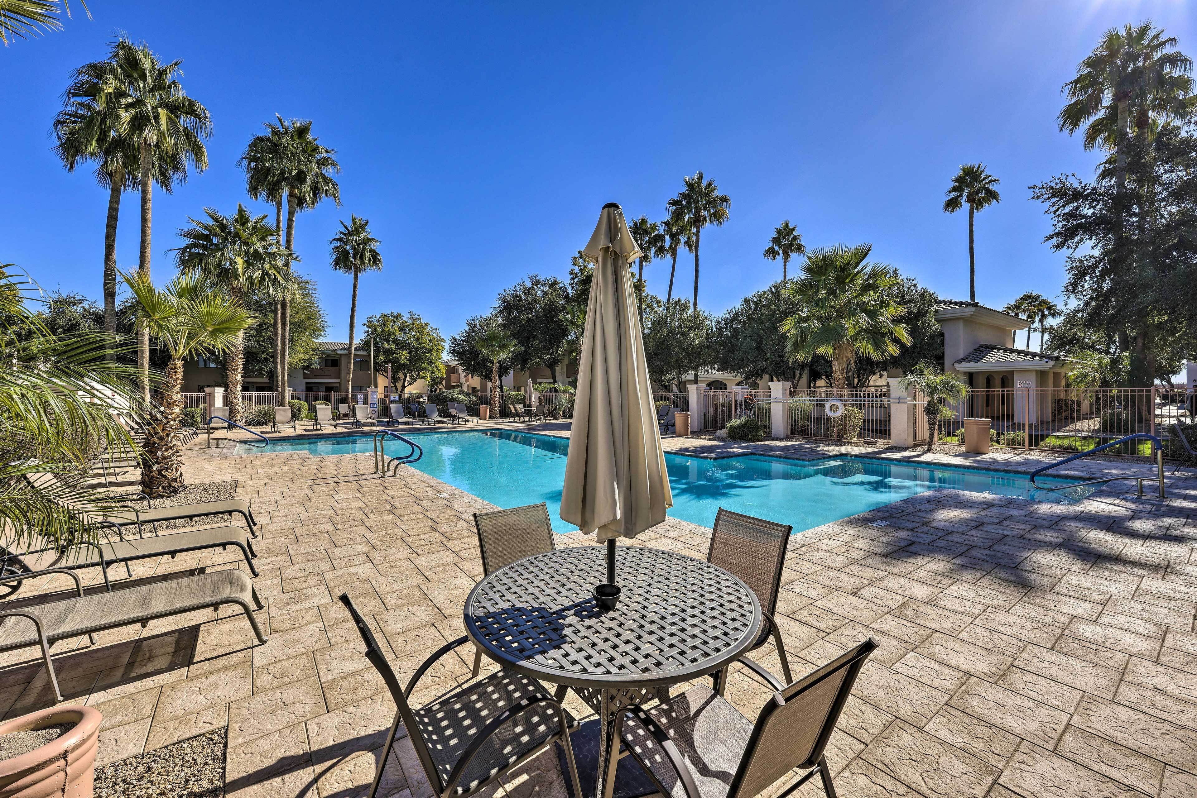 Un espace aménagé au bord de la piscine, avec une table et des chaises, entouré de palmiers et surplombé d’un ciel bleu azur.