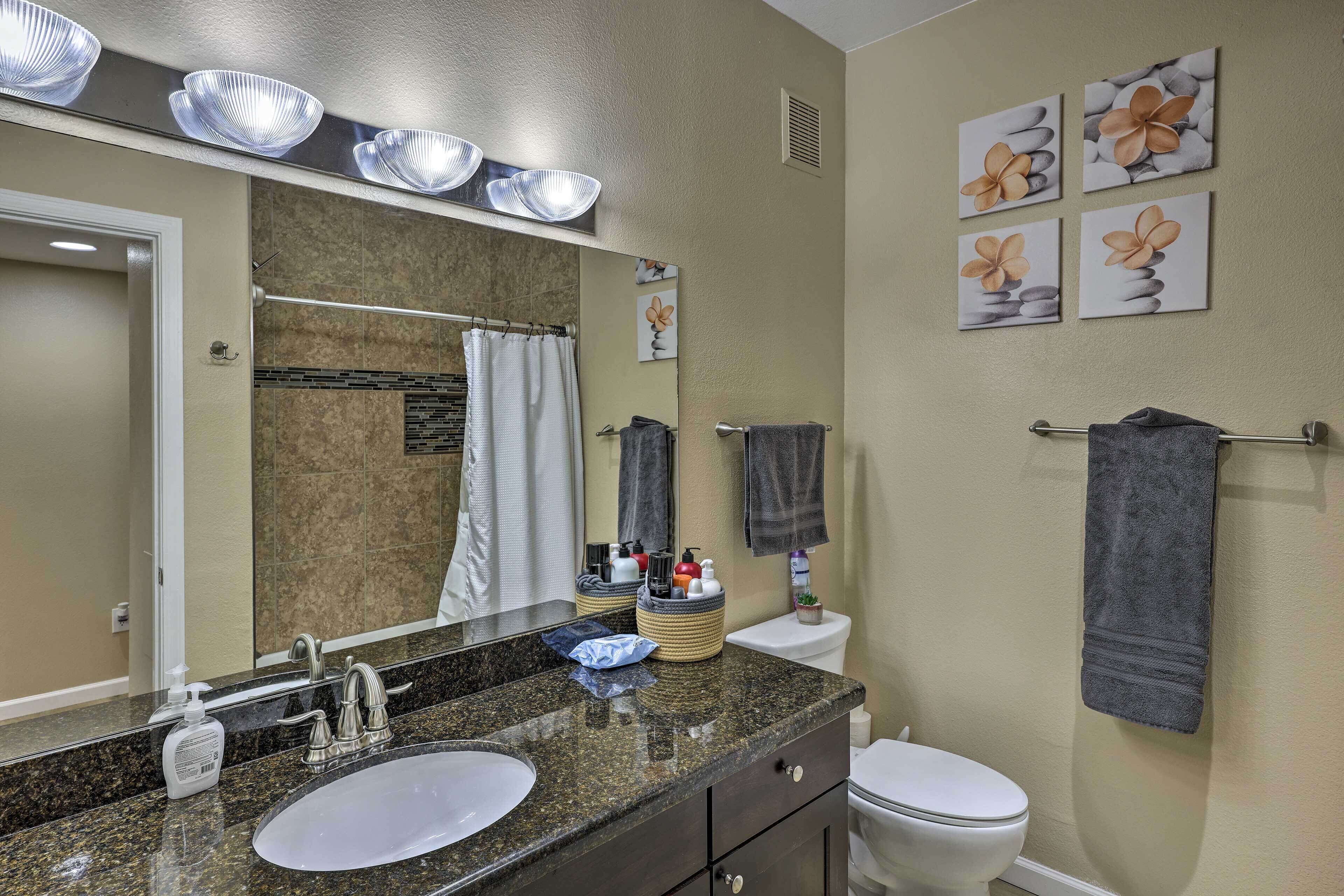 A bathroom with a granite countertop, two sinks, a toilet, and a towel rack.