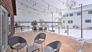 Une terrasse en bois avec des sièges d’extérieur, une vue sur un paysage enneigé et un bâtiment blanc en arrière-plan.