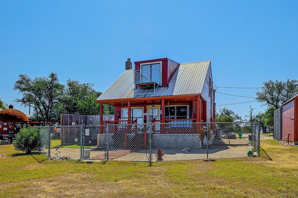 A two-story house with a red and white exterior, a fenced yard, and a small porch. - Pet-friendly Fredericksburg Cabin w/ Hot Tub! (Fredericksburg)
