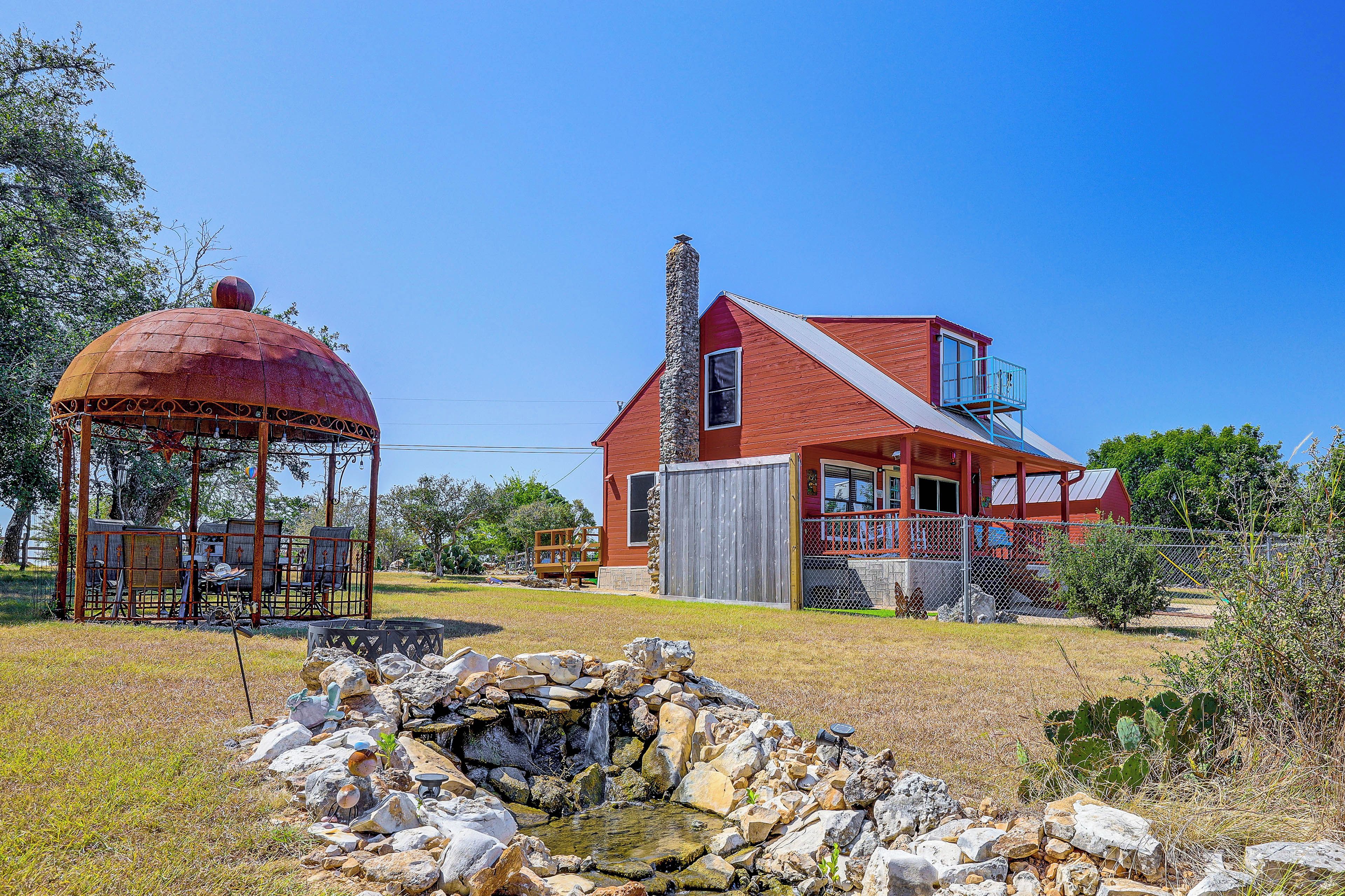 A red house with a stone chimney, a gazebo, and a small pond with rocks.