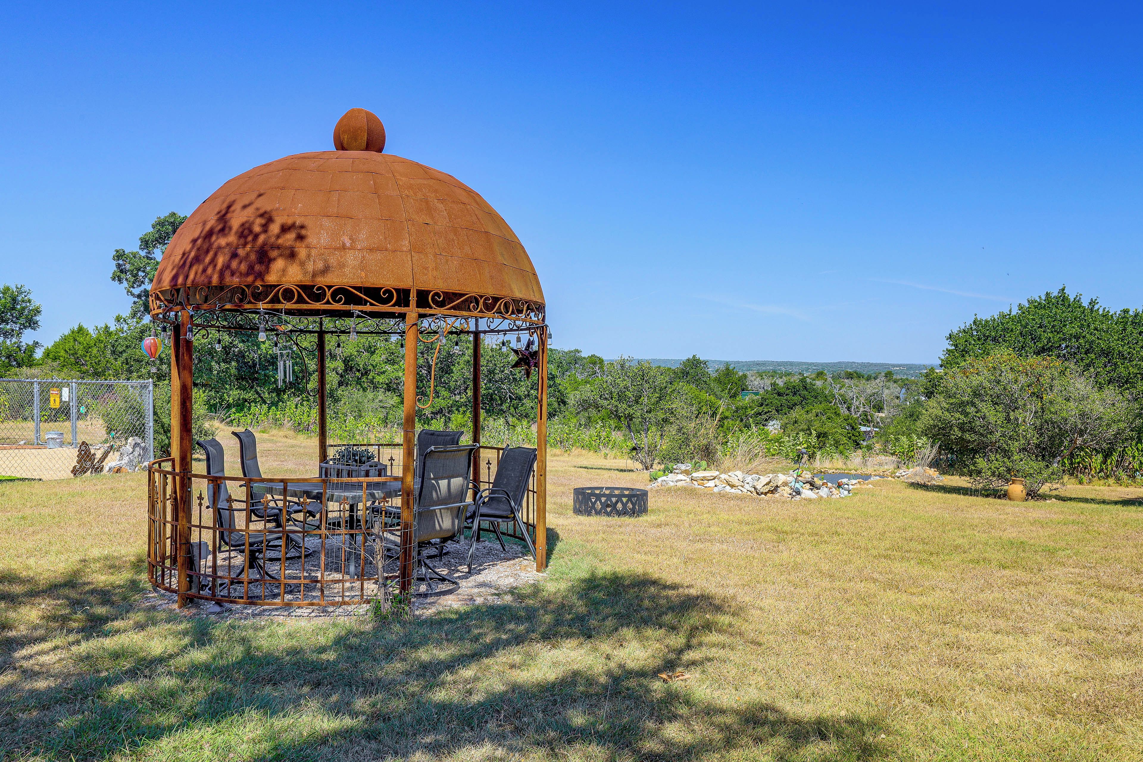 Un gazebo con tetto a cupola e struttura in metallo, circondato da un'area verde con recinzione e alberi.