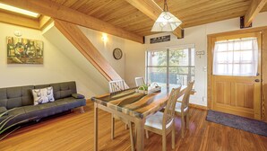 A cozy interior with a wooden ceiling, a dining table with chairs, a sofa with cushions, a wall clock, and a door with a window.