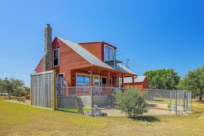 Una casa roja de dos pisos con chimenea de piedra, un balcón y un patio cercado.