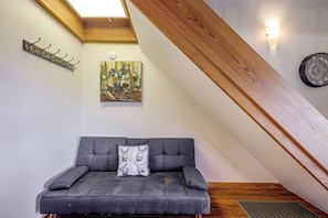 Una habitación estilo loft con un sofá gris oscuro, un cuadro, techo de madera y una lámpara fijada a la pared.
