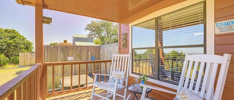 A wooden deck with two rocking chairs and a table, overlooking a fenced yard.