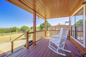 A wooden deck with a rocking chair and a view of the landscape. - Pet-friendly Fredericksburg Cabin w/ Hot Tub! (Fredericksburg)