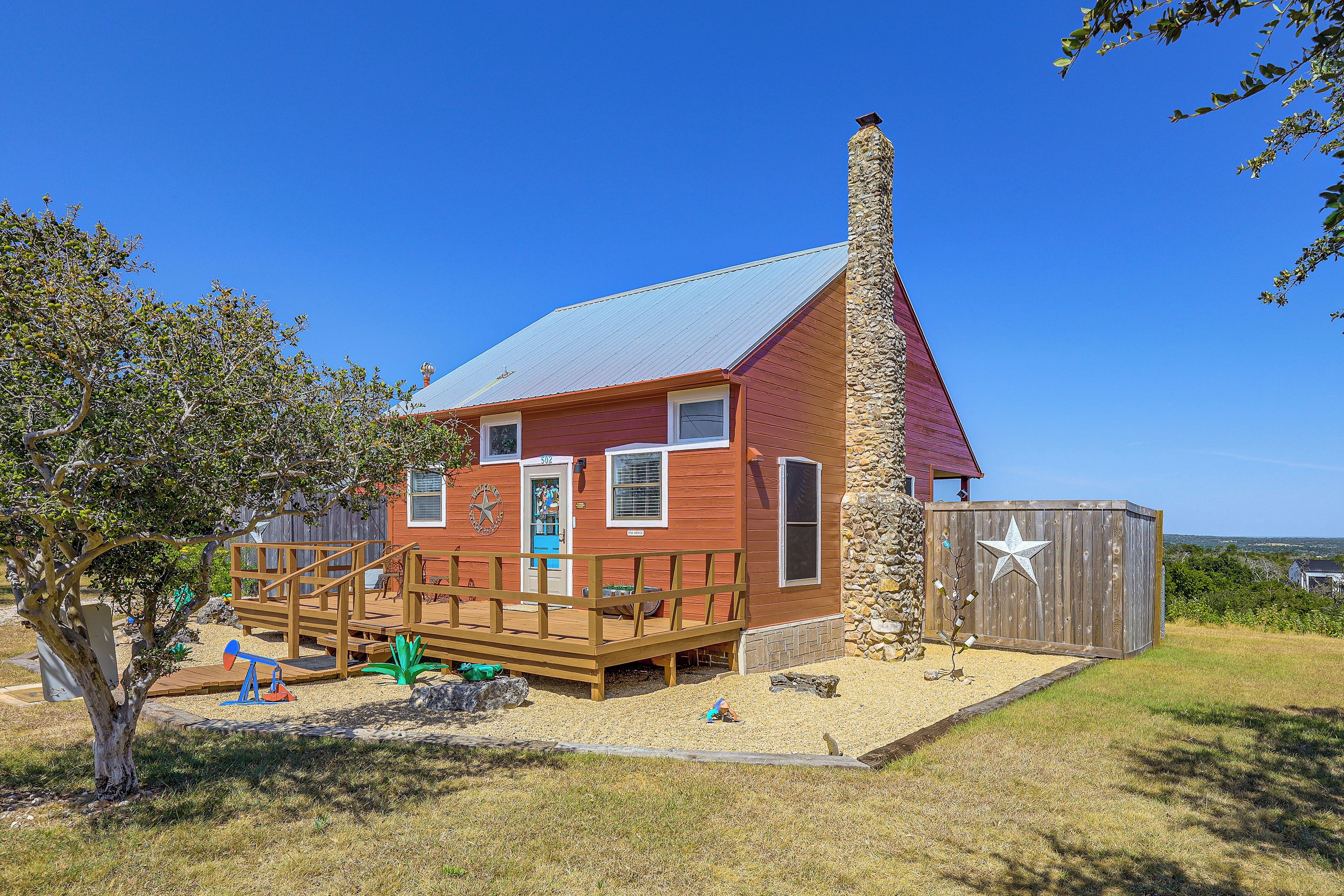 A red wooden house with a stone chimney, a wooden deck, and a fenced yard.
