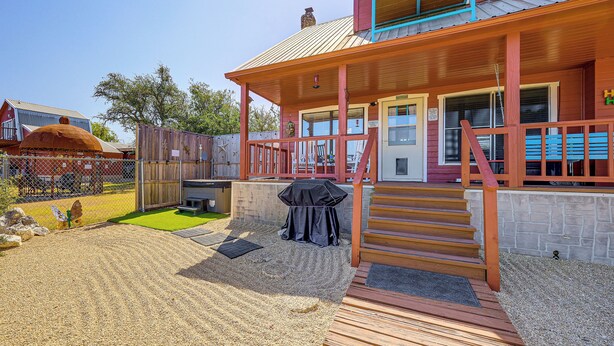 A two-story building with a porch, a barbecue grill, and a stone wall.
