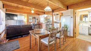 A cozy interior with a wooden ceiling, a dining area with a table and chairs, a sofa, and a kitchen in the background. - Pet-friendly Fredericksburg Cabin w/ Hot Tub! (Fredericksburg)