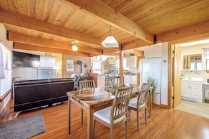 A cozy interior with a wooden ceiling, a dining area with a table and chairs, a sofa, and a kitchen in the background. - Pet-friendly Fredericksburg Cabin w/ Hot Tub! (Fredericksburg)