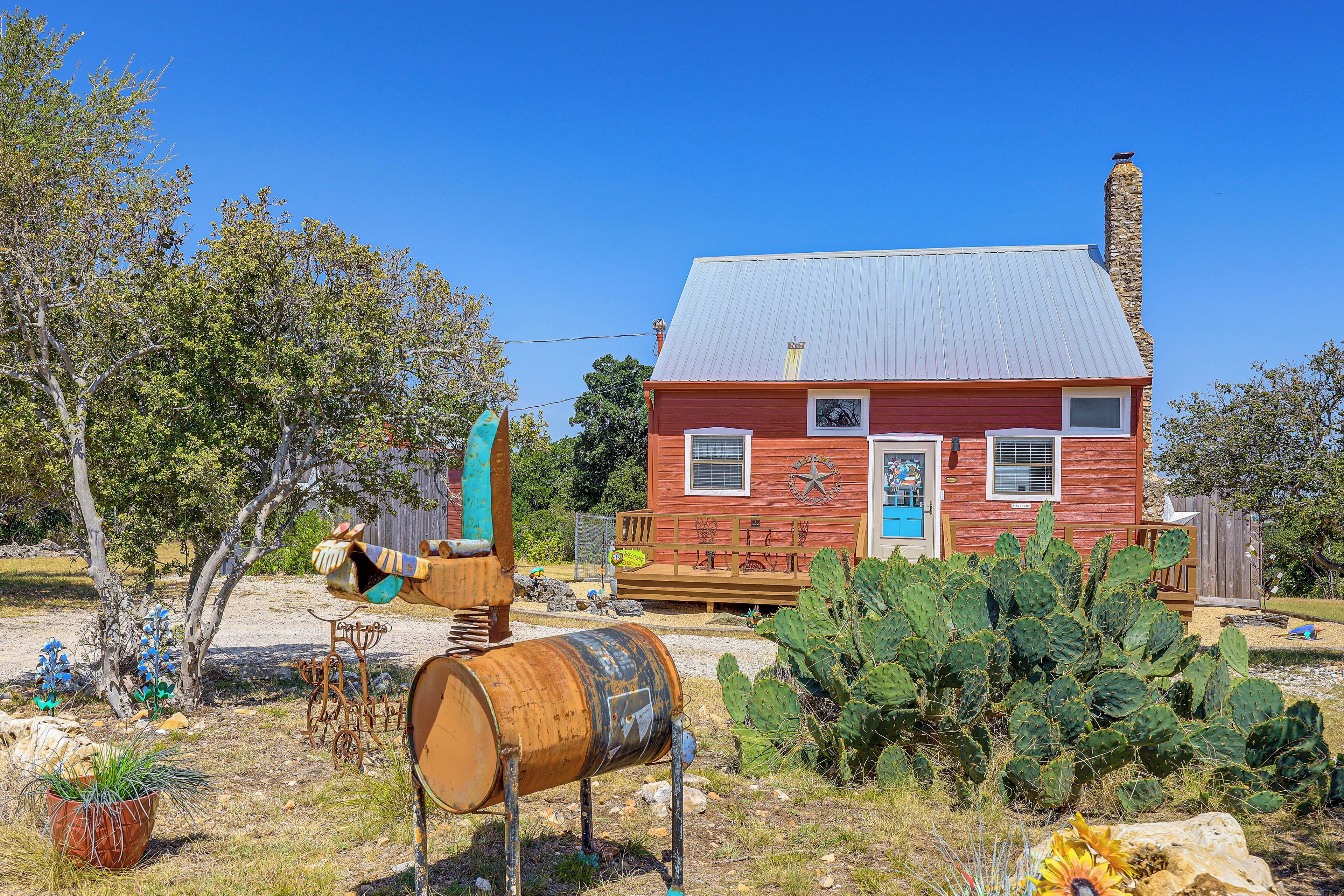 Una casa rústica de color rojo con techo de metal, un porche de madera y un jardín de cactus.