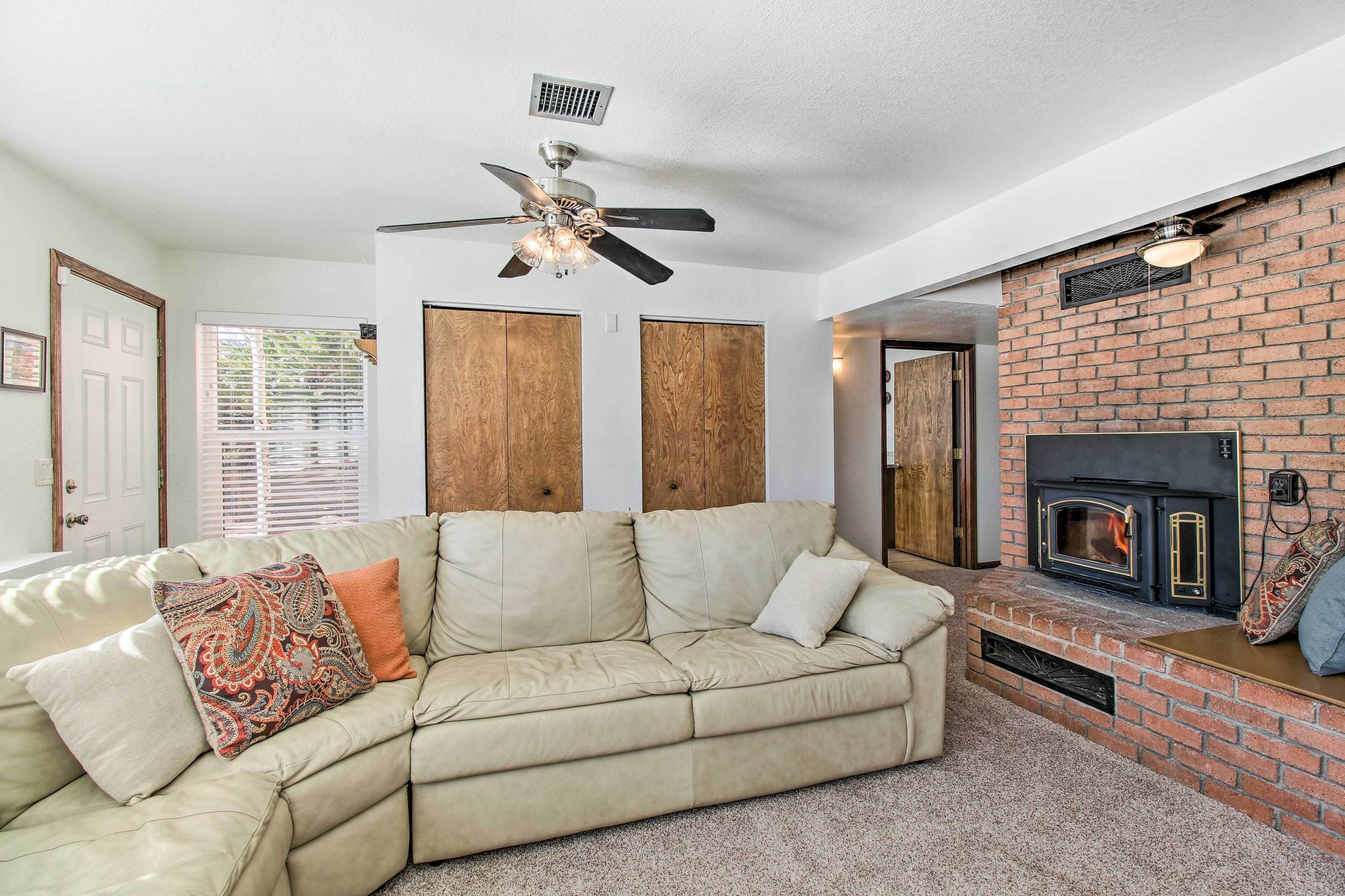 A living room with a beige sectional sofa, a fireplace, and a ceiling fan.