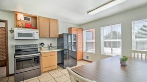 A modern kitchen with stainless steel appliances, wooden cabinets, and a dining area with a table and chairs. - Patio, Grill & Fire Pit: Show Low Escape! (Show Low)