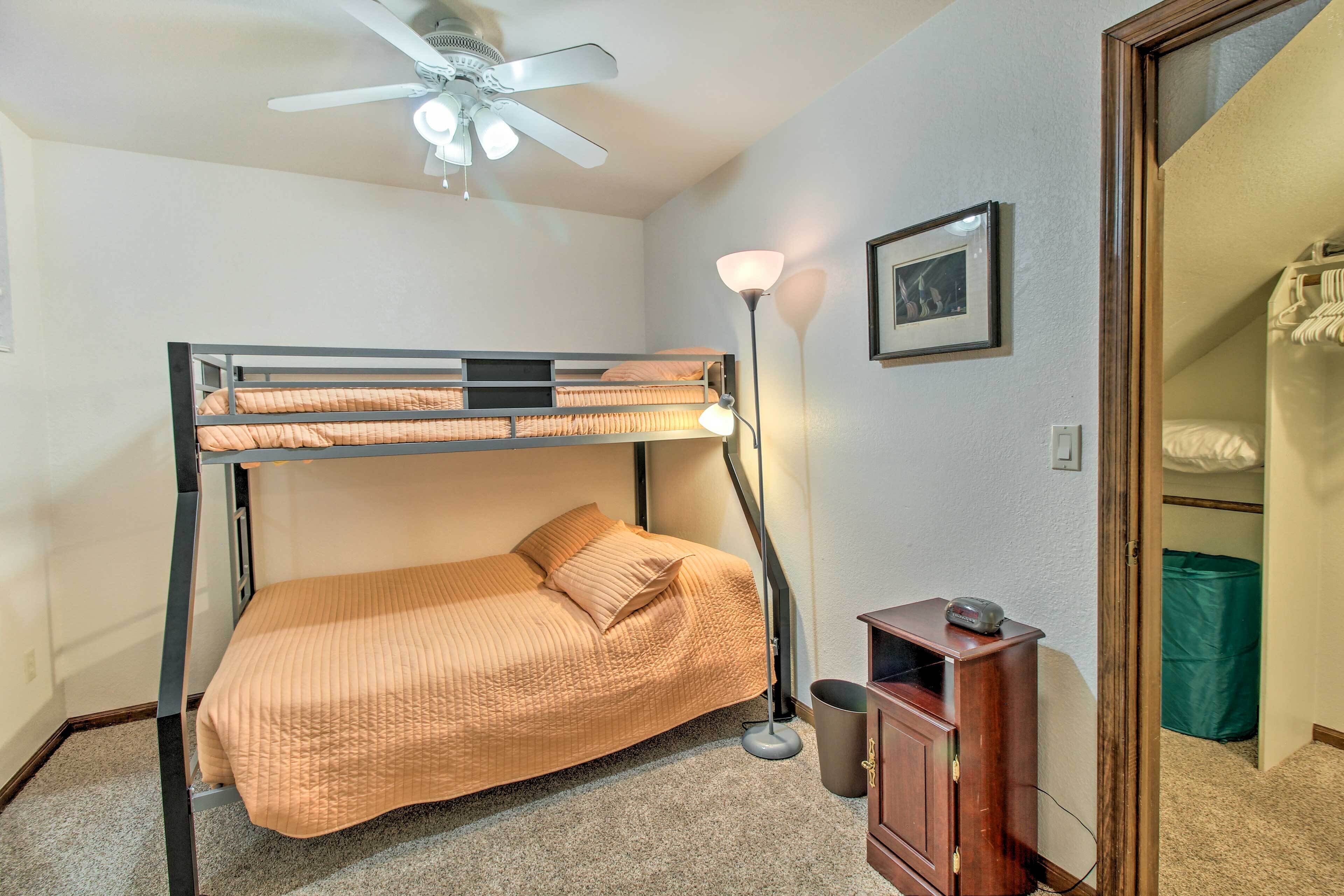 A bunk bed with a ceiling fan, a bedside lamp, and a small cabinet.