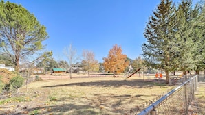 A fenced park with playground equipment, trees, and a clear sky.