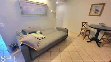 Una habitación con un sofá gris, dos sillas de madera, una mesita redonda y un cuadro en la pared.