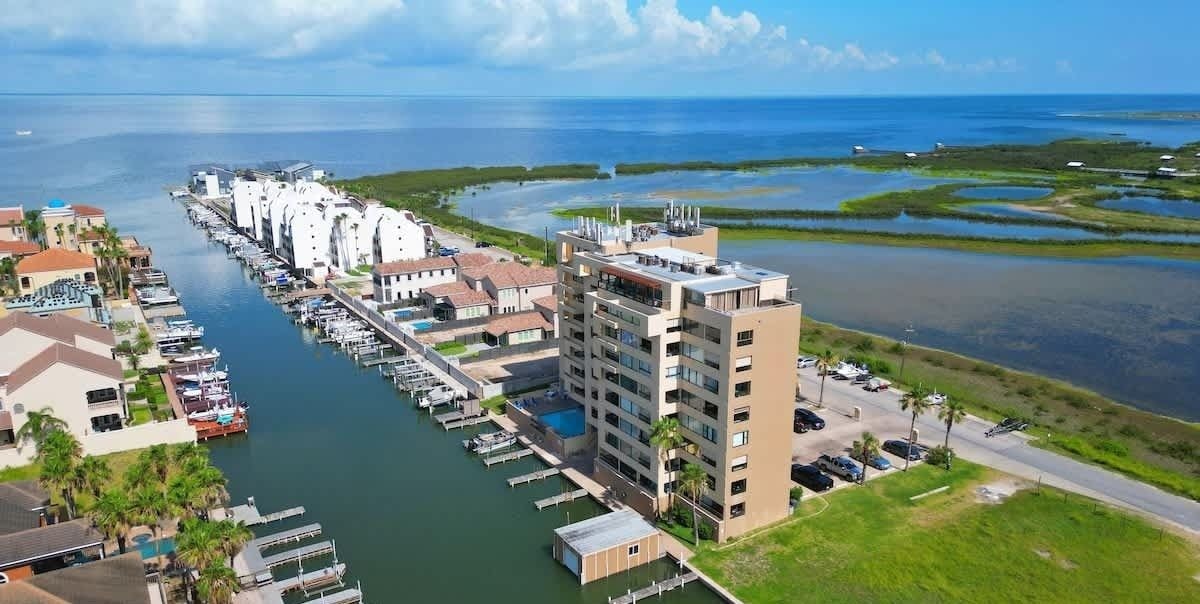 Une vue aérienne d’une marina où sont amarrés de nombreux bateaux, d’un grand bâtiment doté d’un toit plat et d’une vue dégagée sur l’océan.
