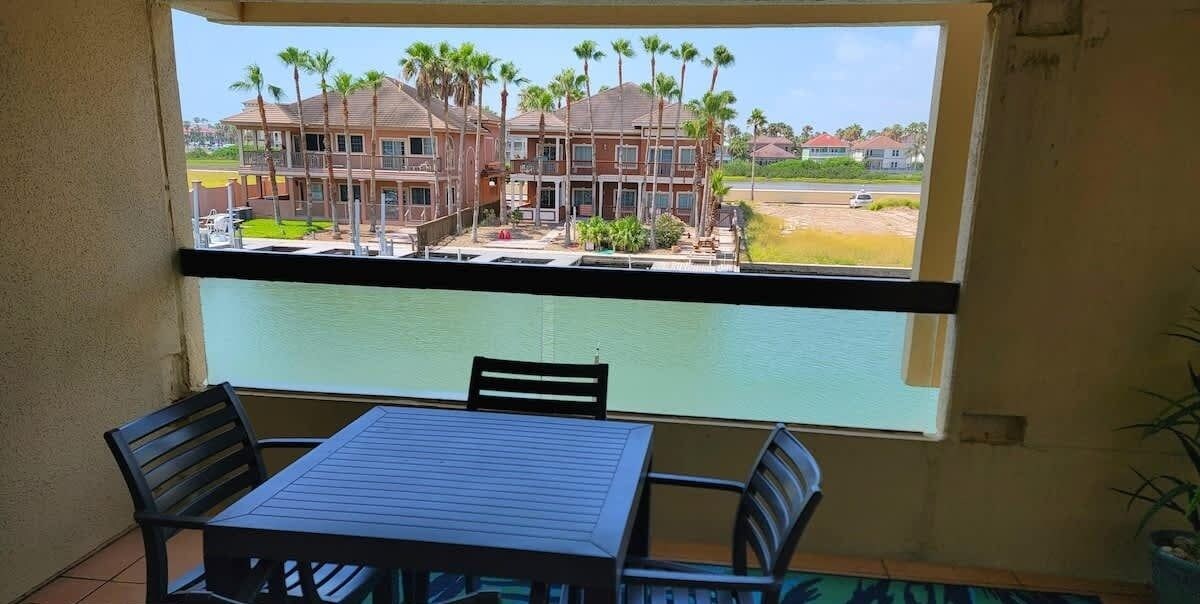 Ein Balkon mit Tisch und Stühlen, mit Blick auf ein Gebäude mit Palmen und einem Schwimmbad.