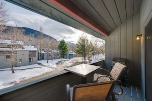 Un balcón con mesa y sillas, con vistas a una calle nevada y edificios.