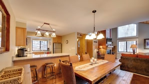 A spacious kitchen with wooden countertops, a large island, and pendant lighting. There is a dining area with a wooden table and chairs, and a cozy seating area with a sofa and cushions.