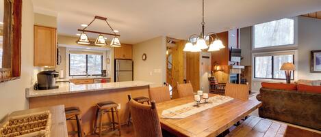A spacious kitchen with wooden countertops, a large island, and pendant lighting. There is a dining area with a wooden table and chairs, and a cozy seating area with a sofa and cushions.