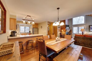 Cocina amplia con encimeras de madera, una isla grande e iluminación colgante. Hay un comedor con mesa y sillas de madera, y un rincón de estar acogedor con sofá y cojines.