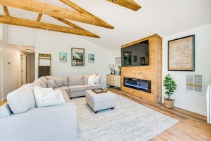 Een moderne woonkamer met een hoekbank, een open haard en kunstwerken in lijsten aan de muren.