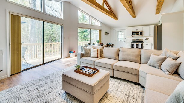 A spacious living room with a large sectional sofa, a wooden ceiling, and a sliding glass door leading to a balcony. - Deck & Community Perks: Bright Pocono Lake Home! (Pocono Lake)