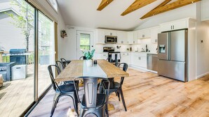 A modern kitchen with white cabinets, stainless steel appliances, and a large wooden dining table. - Deck & Community Perks: Bright Pocono Lake Home! (Pocono Lake)