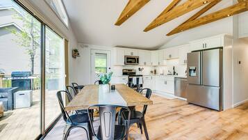 Una cocina moderna con armarios blancos, electrodomésticos de acero inoxidable y una amplia mesa de comedor de madera.