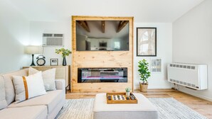 A modern living room with a fireplace, a sofa, a coffee table, and a small plant. - Deck & Community Perks: Bright Pocono Lake Home! (Pocono Lake)